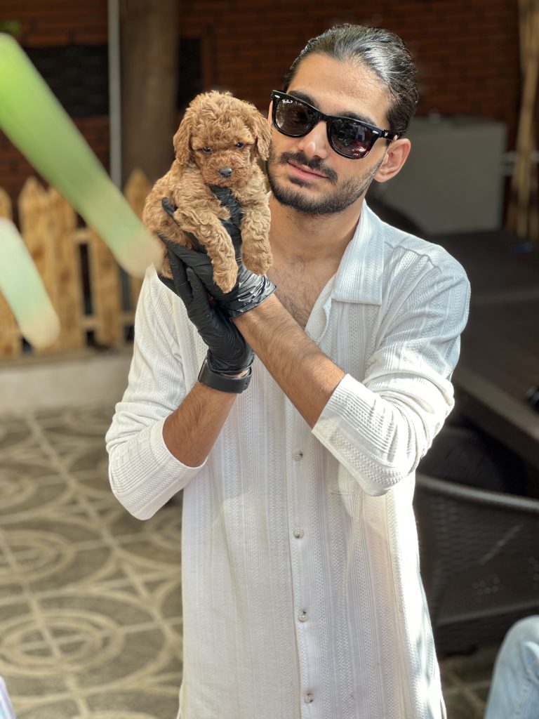 "A man in a white outfit holding a cream-colored poodle."