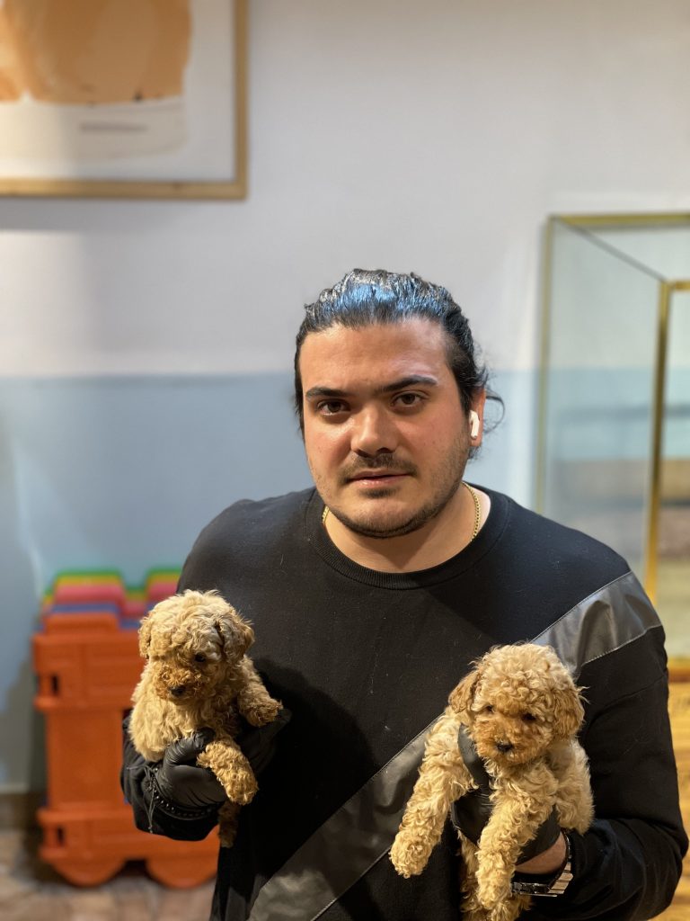 "A man holding two small cream-colored toy poodles in his hands."